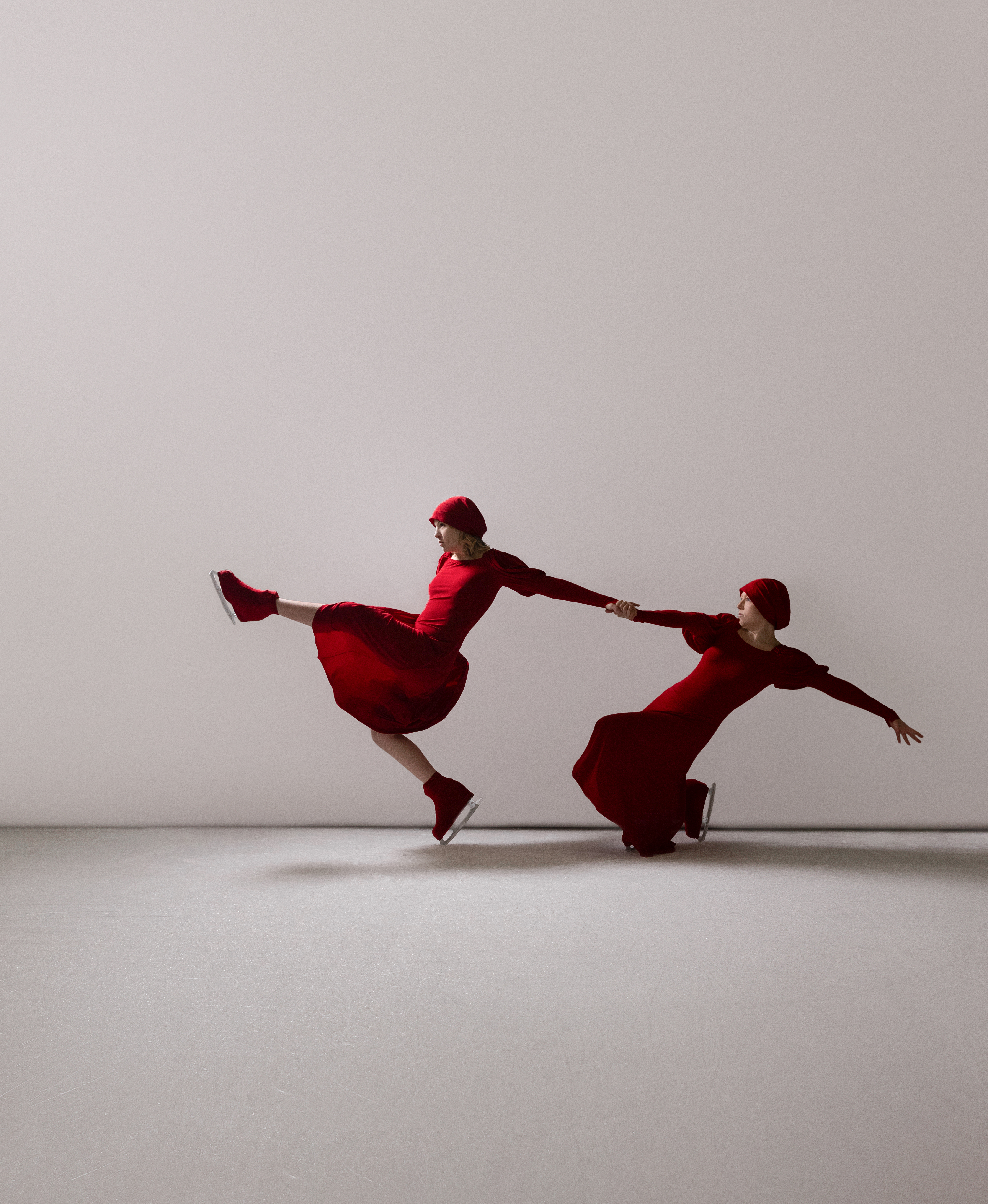 Two skaters in red, connected at hands, pulling apart